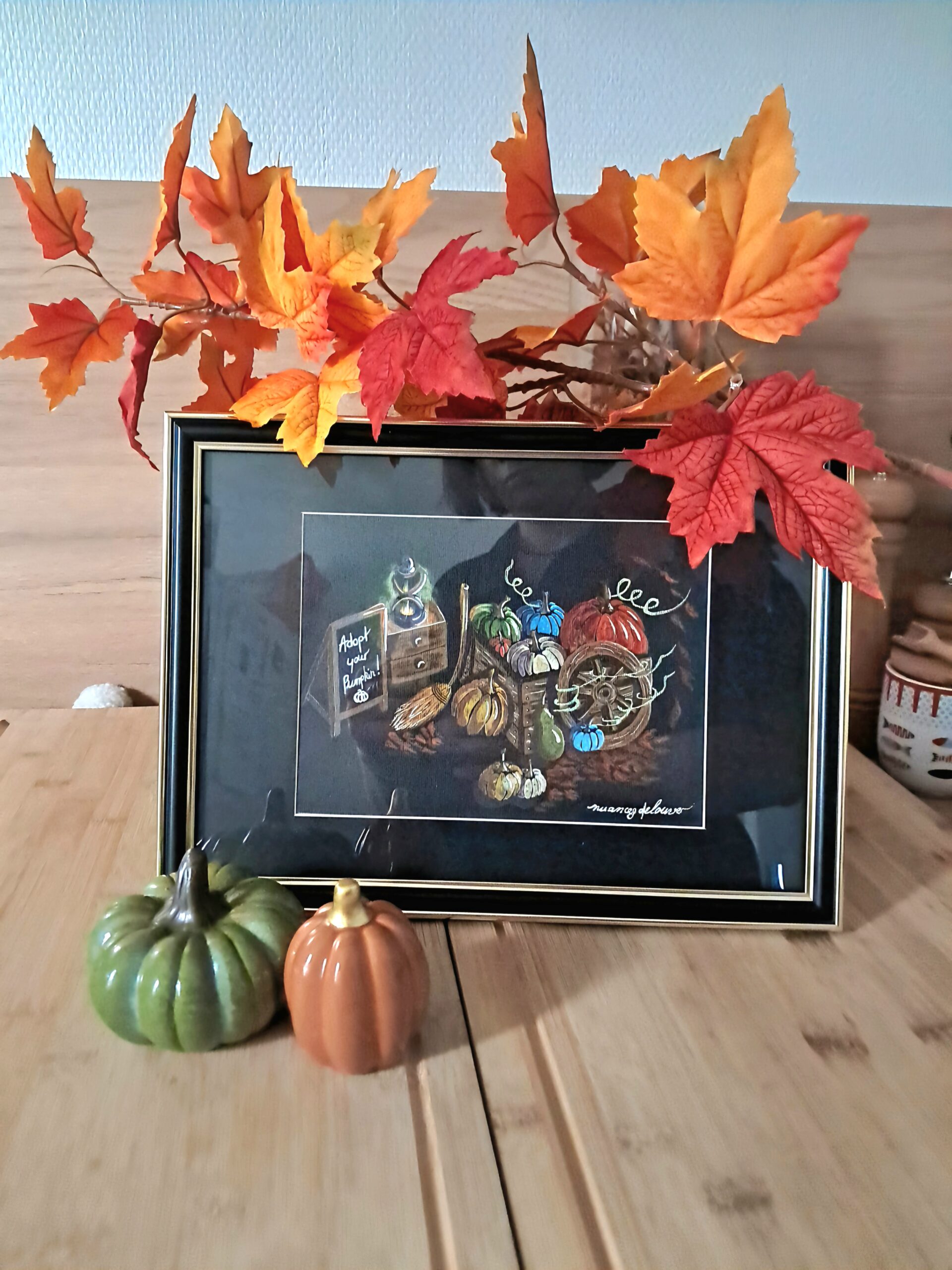 Aquarelle originale "Adopt Your Pumpkin" encadrée et mise en scène avec des feuilles d'automne et des citrouilles décoratives.