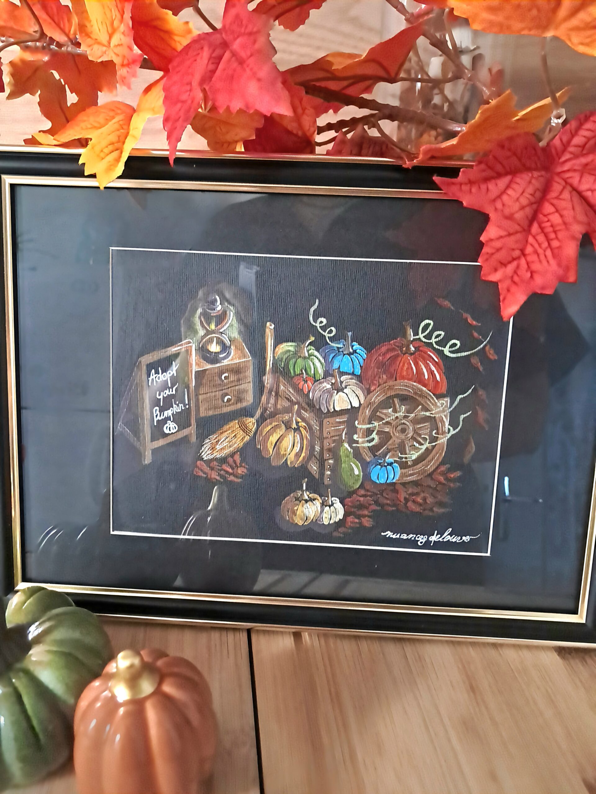 Aquarelle originale "Adopt Your Pumpkin" sur papier noir présentée dans un cadre noir avec passe-partout doré, décorée de feuilles d'automne et de citrouilles