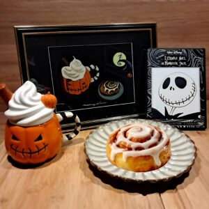 Aquarelle originale The Nightmare Before Michaelmas représentant une tasse citrouille, un cinnamon roll et un écran inspiré de The Nightmare Before Christmas sur papier noir.
